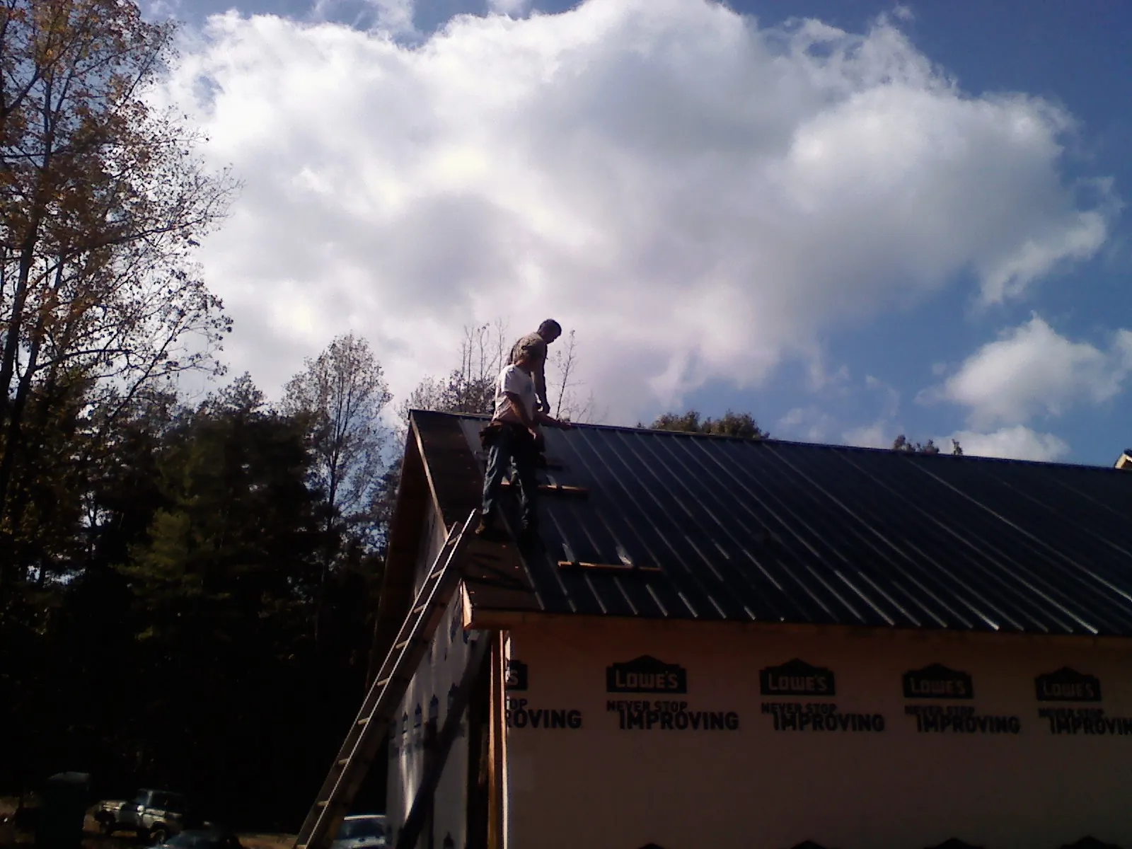 Roofer fastening dark metal panels high against a cloudy sky, from a Roof Inspection job in Ypsilanti